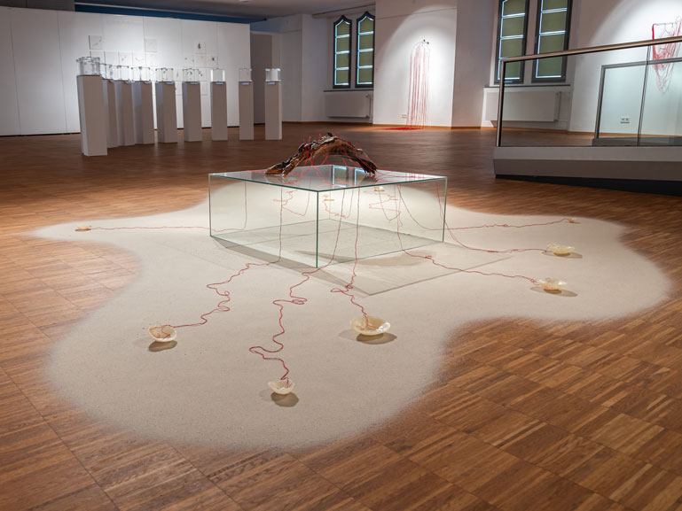 ANJA ASCHE – Entfaltung. 
Installation – Holzstück, Wachs, Fäden, Nadeln, Sand, Podest, ca. 400 x 350 cm, 2023