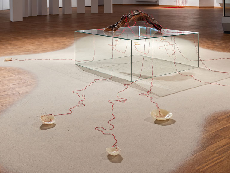 ANJA ASCHE – Entfaltung. 
Installation – Holzstück, Wachs, Fäden, Nadeln, Sand, Podest, ca. 400 x 350 cm, 2023